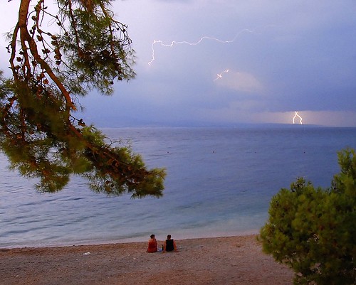 Lightning storm above Hvar island and a couple watching at the beach in Baska Voda