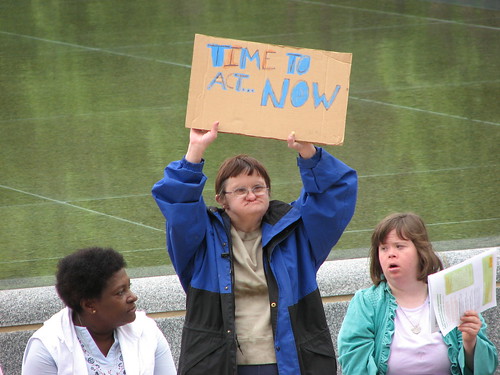 A woman holds up a sign reading Time to act... NOW!
