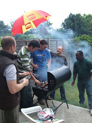 blokes by a barbecue in the rain under an umbrella