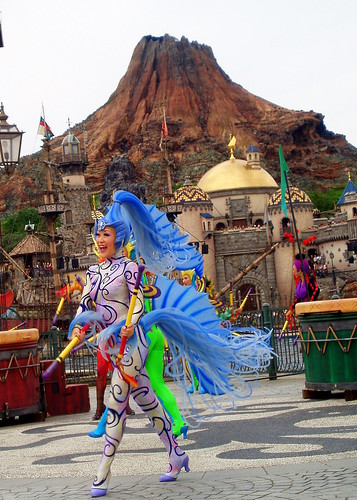 The dancers on shore use their bright colored costumes to attrack attention against the dark background.  Here we have a truly stunning photo of one of the beautifully dressed cast members performing against the parks icon volcano, Mt. Promethus.