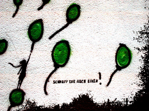 graffiti of green balloons, a person grabbed on to one, next to the words "schnapp dir auch einen!"