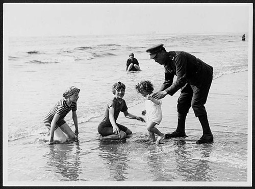 British Tommy interests himself in the happiness of the kiddies on the sands at a French coast resort