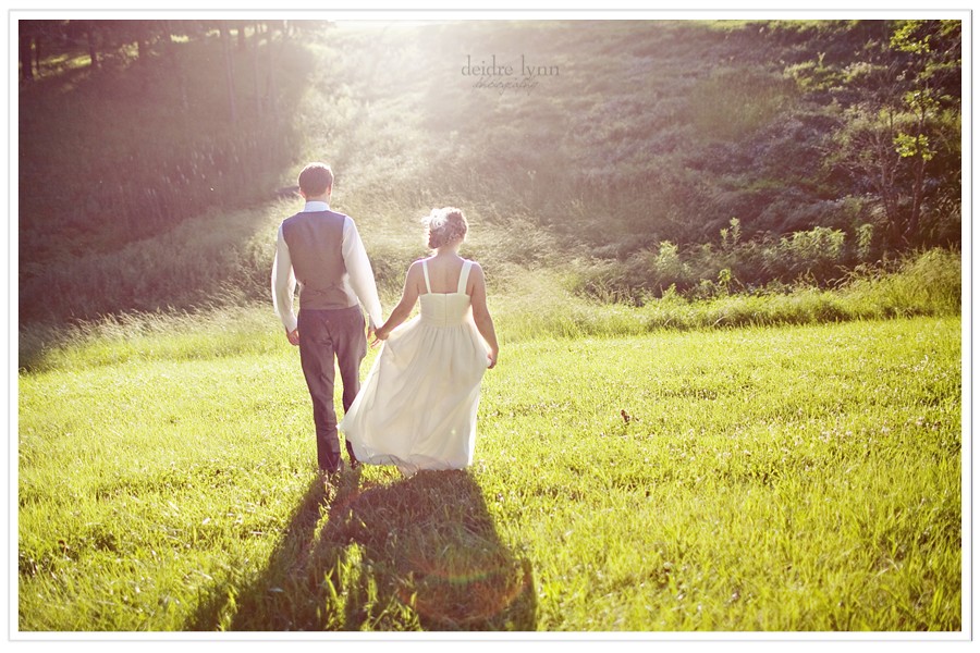 bride and groom walking into sunset in field