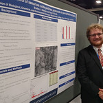 A student posing with his poster at a conference.