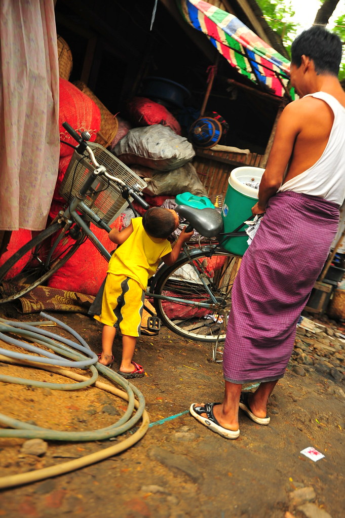 Myanmar strength training: 4 year old boy tries to hold up bike as father looks on.