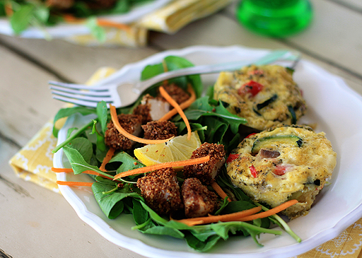 two zucchini frittata muffins on a white plate with a side salad. 
